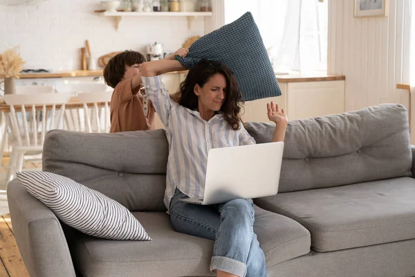 Kid molestar a mamá del trabajo lucha con almohada irritar a la madre en cuarentena. Familia encierro estilo de vida — Foto de Stock