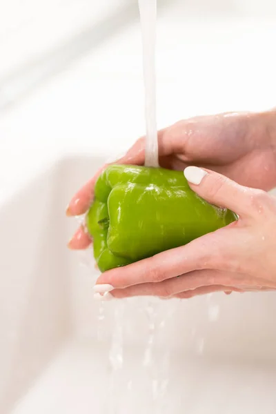 Laven antes de comer: la hembra que lava el pimiento verde en el agua en el fregadero antes de cocer la ensalada. Concepto de higiene —  Fotos de Stock