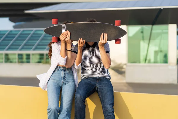 Fröhliches Paar küsst sich über Longboard. Verspielter Mann und verliebte Frau halten Skateboard zusammen — Stockfoto