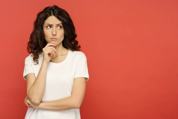 Portrait of doubtful young female pensive think with folded arms look up over red studio background — Stock Photo, Image