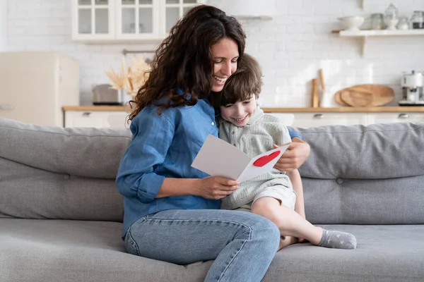 Žena maminka dostat dárek od dítěte: šťastný maminka těšit čtení přání od malého syna na matka den — Stock fotografie
