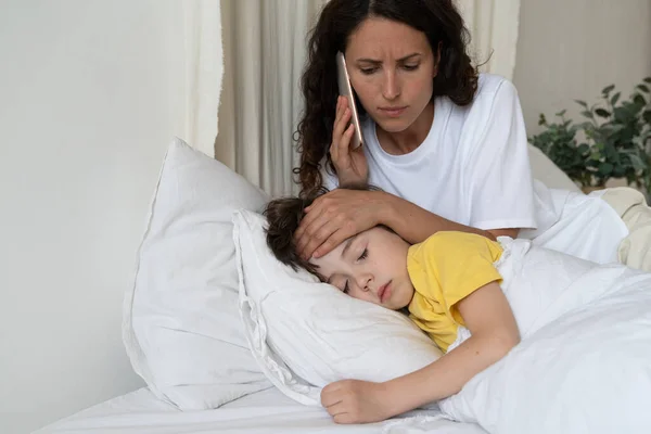 Worried mother call to doctor checking temperature of sick kid lying in bed. Child cure and health — Stock fotografie