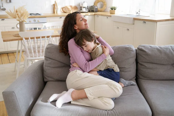 Caring mother and preschool kid boy sit on couch hugging with closed eyes. Family love and bonding — Stock Photo, Image