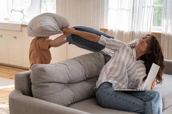 Frustrovaná máma praštila hravé dítě polštářem za vyrušení z práce. Máma se snaží používat notebook doma — Stock fotografie