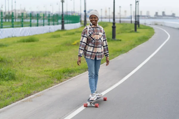 Mutlu, afro bir kadın, kaykay yaparken gülümsüyor. Kaykayla şehir dışında rahatlıyor. — Stok fotoğraf