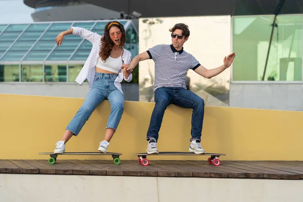 Молода пара хіпстерів розважаються з дошкою, вдаючи їздити скейтборд, сидячи в міському скейтпарку — стокове фото