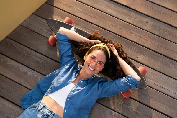 Mujer sonriente sin preocupaciones en el monopatín relajado y feliz. Chica de moda skateboarder acostado en longboard — Foto de Stock