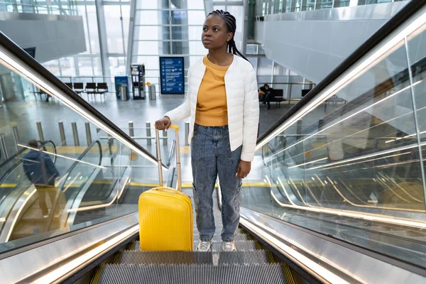 Black woman tourist with suitcase on escalator in airport or train station travel