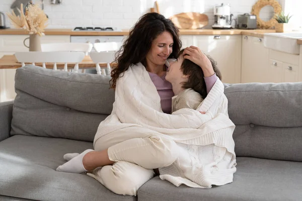 Happy mom spend time with child at home on weekend embrace boy laughing under blanket sit on sofa — Stock Photo, Image