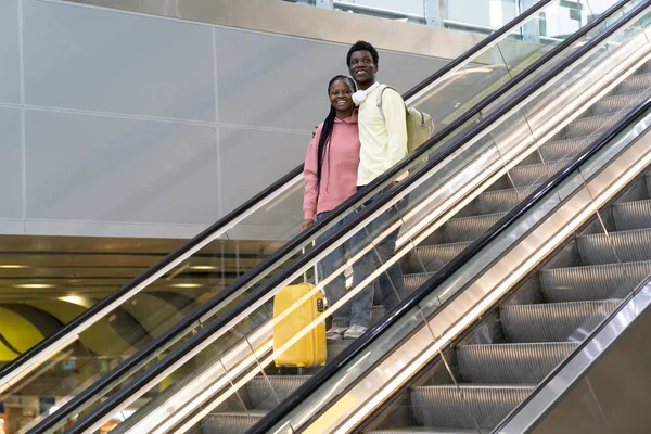 Couple africain souriant dans le stand de l'aéroport sur l'escalator avec voyage valise après la fin verrouillage covid — Photo