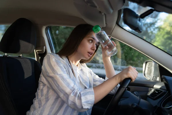 Chica agotada conductor que sufre de dolor de cabeza, calor, clima caliente aplica botella de agua a la frente — Foto de Stock