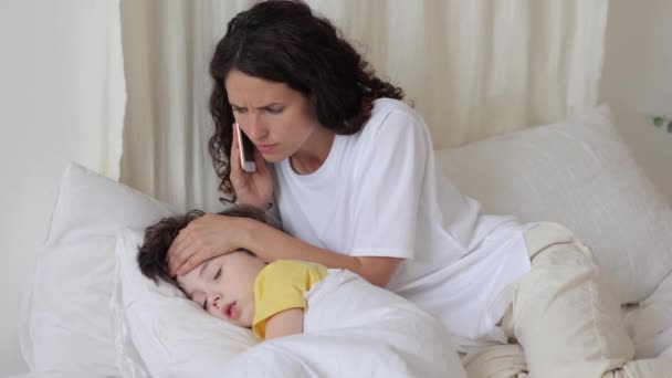 Preoccupato mamma chiamata medico toccare bambino caldo fronte misurare la temperatura del bambino come malato ragazzo dormire a letto — Video Stock
