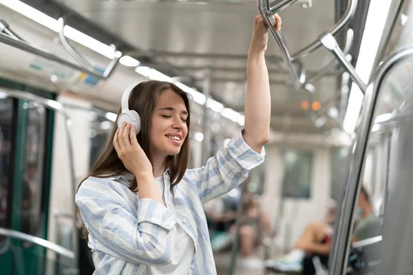 Carefree millennial linda chica pasajero escuchando música con auriculares inalámbricos en tren subterráneo. — Foto de Stock