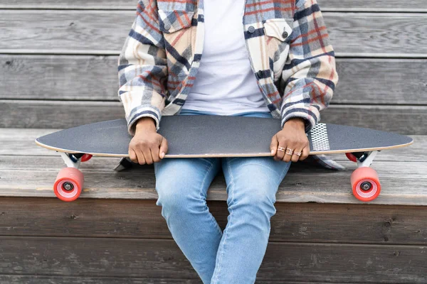 Ethnische Afrikanerin in Freizeitkleidung hält Longboard auf Holzbank mit Skateboard in der Hand — Stockfoto