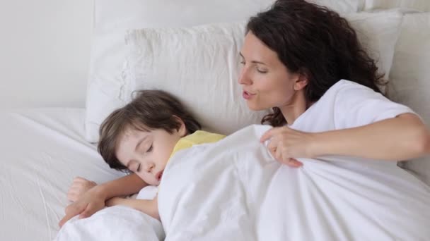 Ibu peduli berpelukan dengan anak laki-laki di tempat tidur menutupi anak laki-laki tidur dengan selimut hangat stroke dan membelai kepala — Stok Video
