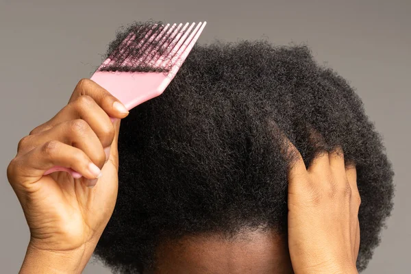 Közelkép afrikai nő segítségével fésű, kefe göndör trükk haj elszigetelt stúdió szürke fal. — Stock Fotó