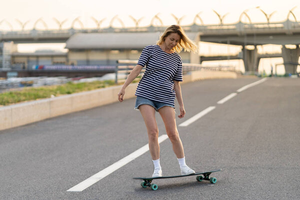 Active adult woman longboarder riding longboard on empty road. Female relax on skateboard after work