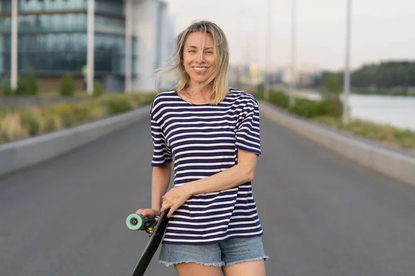 Glad kvinna i medelåldern lycklig efter skateboard. Glada blond kvinna i 40-årsåldern håller longboard — Stockfoto