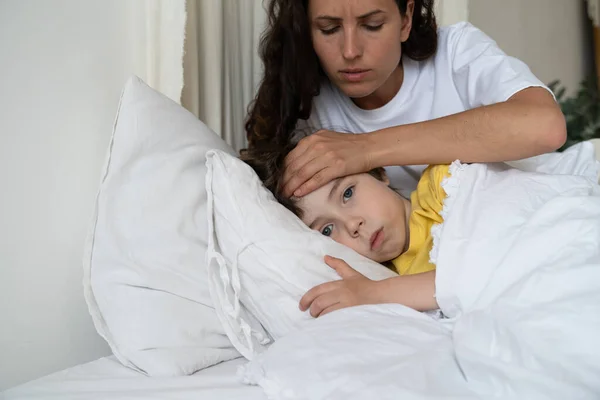 Matko pečující o nemocného syna, zkontrolujte teplotu dítěte, dotkněte se rukou čela. Koncept dětské zdravotní péče — Stock fotografie