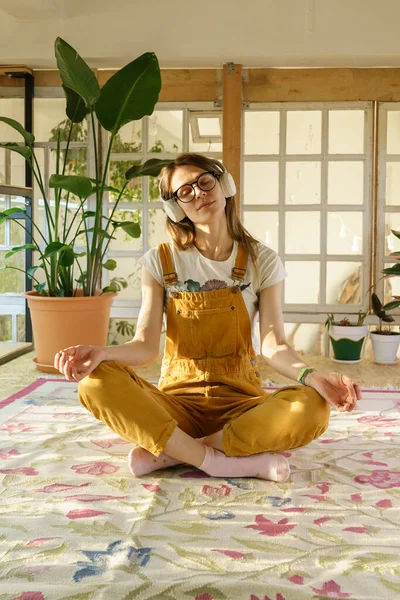 Jóvenes jardineras meditan. Hermosa hembra en mono y auriculares relajarse del estudio o el trabajo — Foto de Stock