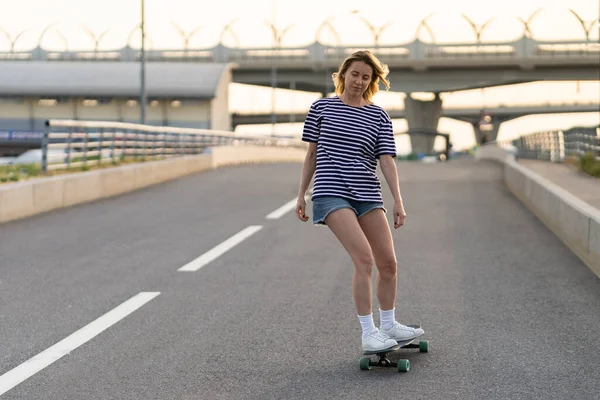 Active adult woman longboarder riding longboard on empty road. Female relax on skateboard after work — Stock Photo, Image