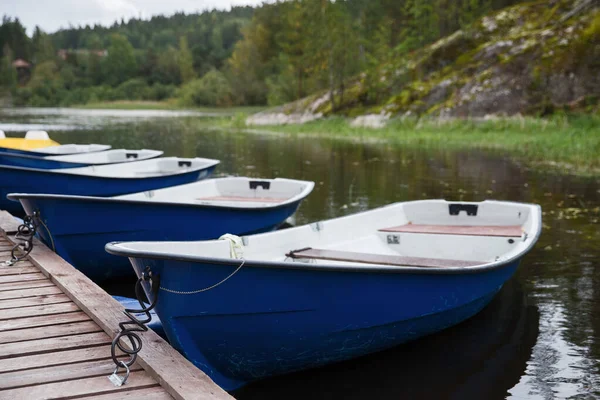 Blue empty boats on the lake along the wooden pier closeup, cloudy autumn sky and forest on background . Recreational row boats. Boat rental