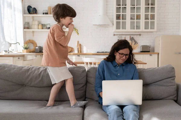 La jeune femme stressée travaille à la maison sur un ordinateur portable fatigué stressé par un petit enfant désobéissant hyperactif — Photo