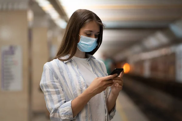 Woman wear face mask using cellphone chatting in social media waiting for subway train on platform