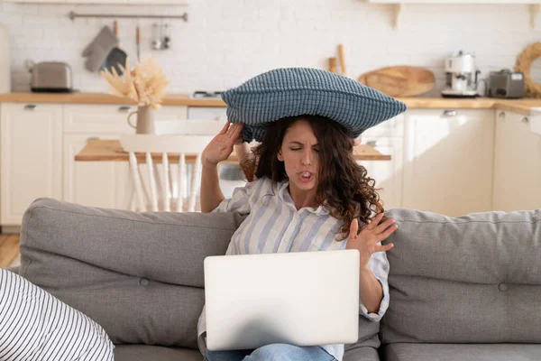 Boos jong mam proberen te concentreren op het werk in laptop als kleine ongehoorzame kind sloeg haar met kussen — Stockfoto