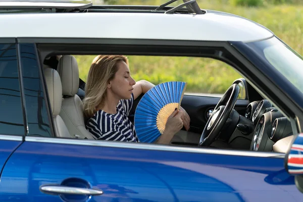 Žena řidič s ruční ventilátor trpí teplem v autě, má problém s nepracující klimatizací — Stock fotografie