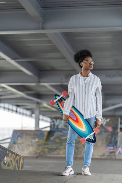 Trendy Αφρικής γυναίκα κατέχουν longboard στην αστική skatepark. Skater κορίτσι της μικτής φυλής σε casual ρούχα — Φωτογραφία Αρχείου