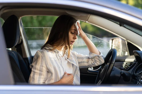 女性ドライバーは車の中で熱波の間に熱くなり、暑い天気に苦しんで額から汗を拭く — ストック写真