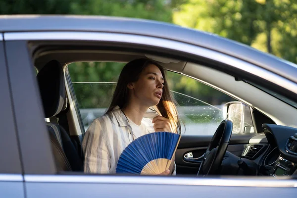 Dívka řidič s ruční ventilátor trpí teplem v autě, má problém s nepracující klimatizací — Stock fotografie