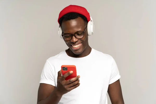 Black male luistert naar muziek in draadloze koptelefoons met behulp van sociale media in smartphone. Studioshoot. — Stockfoto