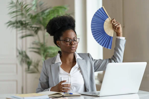 Erschöpfte Geschäftsfrau müde von Hitze winkt Papierventilator für frische Luft bei der Arbeit am Arbeitsplatz Laptop — Stockfoto