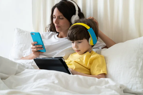 Lazy mum and kid spent morning lying in bed do shopping online in phone and play games on tablet