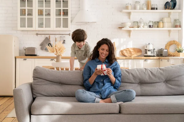 Feliz mamá sentada sosteniendo la caja de regalo en las manos. Hijo preescolar cariñoso saludando a la madre cariñosa en el día de la madre —  Fotos de Stock