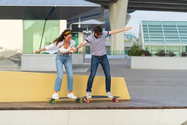 Active young skaters couple learn to ride longboard together hold hands laughing stand on skateboard