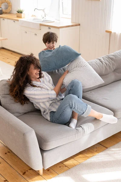 Rire mère célibataire et petit fils s'amusent ensemble heureux jouer combat d'oreillers enfantin dans le salon — Photo