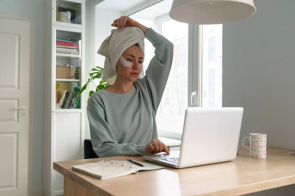 Жінка друкує електронну пошту на ноутбуці працює віддалено з дому в ранковий рушник на латках для догляду за волоссям і шкірою — стокове фото