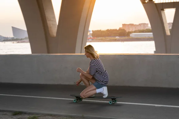 Sport vrouw maken trucs op longboard paardrijden skateboard voor ontspanning of actieve hobby bij zonsondergang — Stockfoto