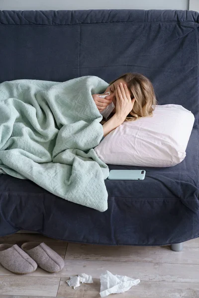 Donna malsana soffre di influenza, allergia fredda o stagionale sdraiata sul divano sotto il naso che soffia coperta — Foto Stock