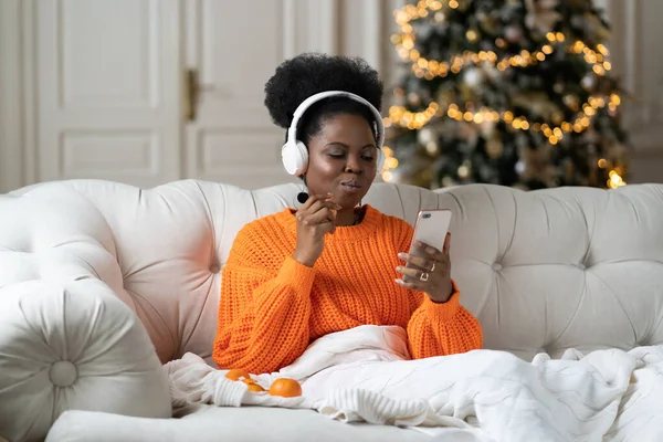 Afrikanerin verbringt Weihnachtsmorgen zu Hause im Wohnzimmer, Weihnachtsbaum liest SMS im Smartphone — Stockfoto