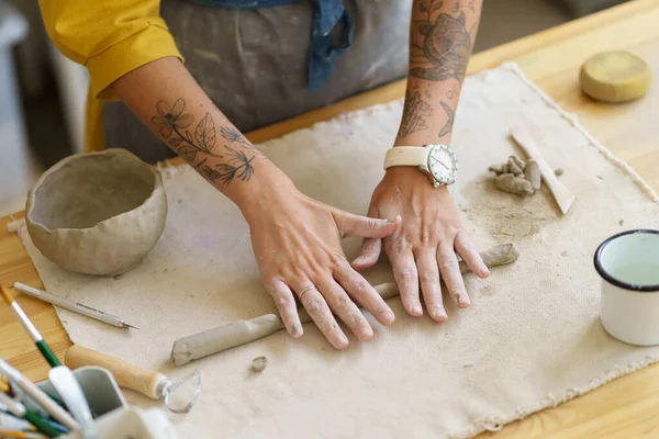 Potter chica rodando pedazo de arcilla con sus manos en la mesa en cerámica, tiene tatuajes en ambos brazos. — Foto de Stock