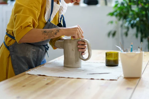 Процес виробництва кераміки ручної роботи: жінка-художник створює глечик з сирої глини, використовуючи інструменти в студії — стокове фото