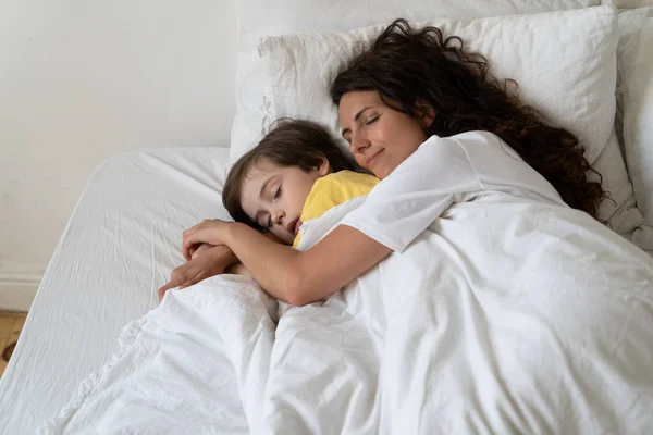 Tranquillo amorevole mamma abbraccio figlio prescolare dormire insieme con il bambino in letto accogliente sotto coperta calda — Foto Stock