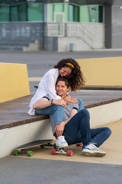 Νεαρό ζευγάρι στην αγάπη απολαμβάνουν ηλιοβασίλεμα κάθονται αγκαλιάζει σε longboard. Μοντέρνο άνδρας και γυναίκα ψύξη εξωτερική — Φωτογραφία Αρχείου
