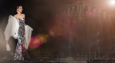 Kabare Karnavalı 'ndaki Asyalı Transseksüel Kadın' ın tam boy vücut portresi. Süslü aynada, arka planda, üç kolaj fotoğrafı olarak, gümüş elbise önlüğünü yansıtıyor.