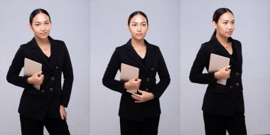 20 'li yaşlardaki Asyalı kadın portresinin yarısı siyah saçlı, resmi takım elbiseli. Ofisteki kadın gri arka planda dijital tablet gülümsemesi taşıyor.