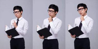 20 'li yaşlardaki Asyalı iş adamının yarı vücut portresi. Siyah saçlı, beyaz tişörtlü. Ofisteki adam duygularını ifade ediyor ve gri arka planda tek başına poz veriyor.